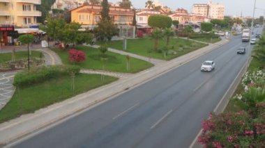 Alanya, Türkiye - 21 Haziran 2019: Güneşli bir günde küçük evler, kesilmiş çimler, bakımlı ağaçlar ve giden arabalar ve otobüslerile düzenli bir caddenin muhteşem manzarası