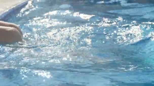女性膝盖和玩腿在游泳池水在夏天的Slo Mo原始特写一个女人坐在游泳池的路边 移动她的腿只是为了娱乐在夏天的阳光明媚的一天在Slo — 图库视频影像