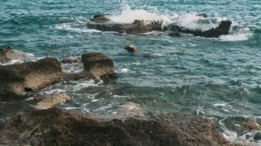 Slo-mo'da yaz aylarında Türkiye'de büyük taşlarla büyük taşlarla akdeniz kıyısı Alanya'da yaz aylarında güneşli bir günde dalgalanan dalgaların etkileyici görünümü yavaş çekimde. 