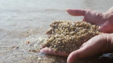 Alanya sahilinde yaz aylarında kum ve kabukları olan iki el, yavaş çekimde iki insan elinin sarı kum ve kabukları sahilde güneşli bir şekilde tutmasının yavaş çekimde