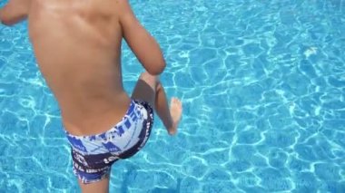 Trunks mutlu çocuk dalış ayakları ilk slo-mo Cheery görünümünde parlayan bir yüzme havuzunda on yaşındaki çocuk su suları ile bir kürek havuzunda ilk ayak atlama. Sıçramaları Yüksek dalga slo-mo sihirli ve ince görünüyor.