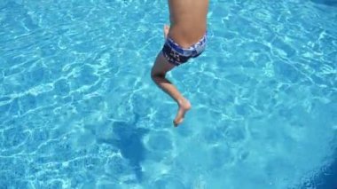 Slo-mo'nun heyecan verici manzarasında, on yaşındaki bir çocuğun gök suları olan bir havuzda ilk olarak ayak atlamasının heyecan verici manzarasında, şortlu küçük çocuk ilk olarak ayak atlıyor. Sıçramaları yüksek dalga slo-mo ilham verici görünüyor.