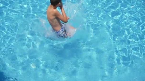 穿着树干潜水膝盖的喜喜男孩首先在Slo Mo游泳池里看到10岁男孩先跳膝盖 在嬉水池里在空中旋转 在波洛莫的海水中闪闪发光 — 图库视频影像
