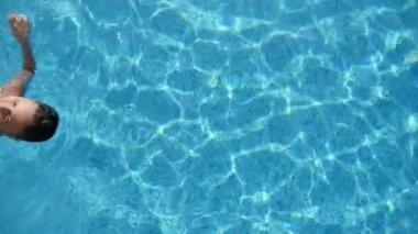 Küçük esmer oğlan yüzme sırtüstü zevk yaşam içinde bir Wading havuz içinde Slo-Mo renkli şort yüzme sırtüstü ve eğlenceli bir Wading gölet turkuaz sularda mutlu küçük bir çocuk neşeli görünümü yavaş hareket.