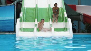 Jolly oğlan ve kız bir üçlü Aqua tüp aşağı sürme içinde Türkiye 'de Slo-Mo yeşil şort ve ince bir kız ib bikini bir neşeli çocuk muhteşem görünümü bir üçlü Aqua tüp üzerinde bir gölet, Slo-Mo kabarcıklar ile mutlu aşağı kayar