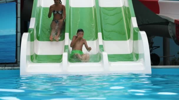 陽気な少年と女の子は 緑のショートパンツで幸せな少年とスタイリッシュな女の子Ibビキニがスロモで水しぶきを持つトリプルアクアチューブのプールで楽しく滑り降りるスロモでトルコのトリプルアクアチューブの上に滑り降りる — ストック動画