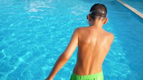 水ゴーグルの陽気な少年は サラダショーツとウォーターゴーグルで幸せなブルネットの少年が最初に足をジャンプし スローモーションのプールで彼の鼻を保つスローモーションでスイミングプールで最初に足をジャンプ — ストック動画