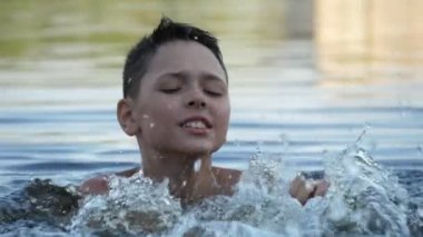 Mutlu çocuk suda duran ve slo-mo bir gölde ilham ile dans Neşeli esmer bir çocuk göl sularında ayakta ve hareketli omuzlar ve slo-mo yaz güneşli bir günde sıçramaları bir sürü mutlu dans komik görünümü