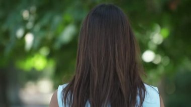 Üst model kız gülümsüyor ve yaz aylarında Slo-Mo etkileyici saç sallayarak uzun gevşek saç biraz gülümseyen ve Slo-Mo yaz aylarında yeşil bir sokakta parlayan gözler ile etrafında saçlarını sallayarak bir üst sınıf esmer kız sanatsal görünümü