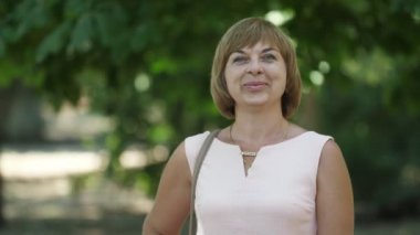 Sevimli sarışın kadın ayakta, gülümseyen ve yaz aylarında bir parkta saçlarını sallayarak bir ışık yaz elbise ayakta Bob saç modeli ile şık bir sarışın kadının Iyimser görünümü, gülümseyen ve yaz aylarında yeşil bir parkta onun saçlarını sallıyor.