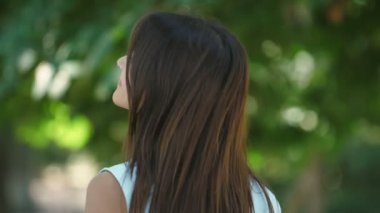 Üst sınıf kız gülümseyen ve şık yaz içinde Slo-Mo ince bir üst model esmer kız zarif gülümseyen ve yaz aylarında yeşil bir sokakta köpüklü gözleri ile saçlarını sallayarak etrafında saç sallayan Arty görünümünde onun başını dönüm Slo-Mo