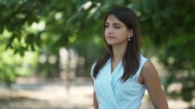 Zarif esmer kız ayakta, bekleyen ve güneşli bir gün yeşil bir sokakta gülümseyen parlak gözleri ve şık bir elbise ayakta uzun gevşek saçlar ile tatlı bir esmer kız neşeli görünümü, onu muhabbetkuşu bekliyor ve yaz aylarında parkta gülümseyen