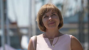 Sarı bir gündüz güneşli bir gün bir liman alanında ayakta gülümseyen sarışın kadın bir Bob saç kesimi ayakta ve duygusal Dnipro dolgu içinde yavaş hareket yaz aylarında güneşli bir gün içinde gülümseyen bir mutlu sarışın kadın, neşeli bokeh portre