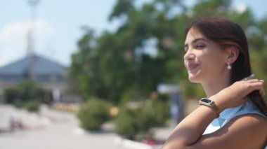 Sevimli esmer kız yürüyüş ve Slo-Mo güneşli bir günde sırıtma geri dönüş uzun gevşek saç ile bir neşeli ve şık esmer kız komik arka görünümü, geri dönüş ve yavaş hareket yaz aylarında yeşil sokakta eleştirel sırıtıyor.