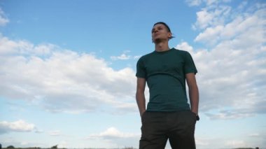 Gülümseyen adam ayakta ve Karadeniz 'de Celeste gökyüzü altında Slo-Mo neşeli bir T-shirt ve siyah pantolon ayakta ve yavaş hareket Karadeniz kıyısında gülümsüyor saç sallayarak emin bir genç esmer adam görünümü aşağı yukarı bakıyor