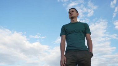 Mutlu adam ayakta ve Karadeniz 'de Celeste gökyüzü altında Slo-Mo görünümlü bir T-shirt ve siyah pantolon ayakta ve siyah deniz sularında Celeste gökyüzü altında Slo-Mo altında zevk saç sallayarak bir sportif genç adamın görünümünü aşağı çarpıcı