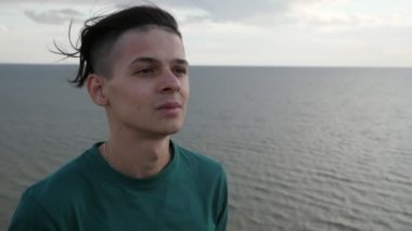 Karadeniz kıyısında duran ve Slo-Mo görünümü zevk sevimli genç adam siyah deniz kıyısında yeşil bir T-shirt ayakta ve Slo-Mo yaz aylarında dalgalar bakarak kısa bir saç kesimi ile gülümseyen genç esmer adamın etkileyici görünümü