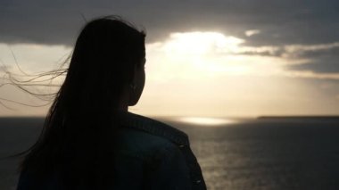 Güzel kız siyah denizde yaz aylarında gün batımında onun geleceği hakkında düşünme Slo-Mo uzun gevşek saç ve derin gözler uçan ile neşeli ve şık genç kadının çarpıcı görünümü yaz aylarında gün batımı içinde onun gelecekteki hayatını düşünme Slo-Mo