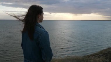 Havadar esmer kız ayakta ve SLO-MO içinde Karadeniz 'de parlayan günbatımı zevk kot pantolon ve kolsuz gömlek uzun gevşek saç sallayarak güzel esmer kız Inanılmaz görünümü Slo-Mo gün batımı Karadeniz dalgalarında ilham alma
