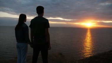 Romantik çocuk ve onun güzelliği gelecekte Karadeniz 'de günbatımında Slo-Mo muhteşem görünümü sevgi ayakta genç bir çift, eller bir arada tutmak ve siyah deniz ufukta yaz aylarında gün batımı içinde geleceği hakkında düşünme bakarak Slo-Mo