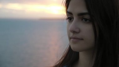 Güzel genç kadın siyah deniz kıyısında yaz aylarında günbatımında duran Slo-Mo siyah deniz kıyısında uzun gevşek saçlı duran tatlı bir genç kadının harika görünümü yaz aylarında muhteşem günbatımı kırmızı bir güneş yolu ile yavaş hareket