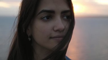 Slo-Mo yaz aylarında gün batımı siyah deniz plajda ayakta Dainty esmer kız uzun gevşek saç ve dipsiz gözleri siyah deniz sahilinde yavaş hareket yaz muhteşem bir gün batımı ayakta sallayan ile tatlı bir genç kadının güzel görünümü