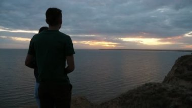 Mutlu çocuk ve güzel kız ayakta, Slo-Mo güzel arka görünümünde siyah deniz günbatımı bakıyor ve uzun gevşek saç ayakta ve Slo-Mo Karadeniz 'de köpüklü günbatımı zevk ilham genç esmer adam ve onun bal kız