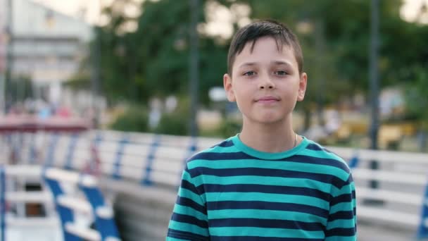 勇敢的布鲁内特男孩站在Dnipro堤上快乐地微笑在夏天的阳光明媚的一天 小布鲁内特男孩与船员理发条纹T恤站立和微笑在Dnipro堤上愉快 — 图库视频影像