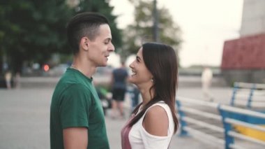 Güzel çift konuşma ve yavaş hareket te dnipro rıhtım da yaz aylarında Dnipro rıhtım üzerinde şaka neşeli sportif genç bir adamın bir T-shirt sohbet ve slo-mo yaz aylarında Dnipro seti üzerinde uzun gevşek saçlı onun bal kız ile şaka