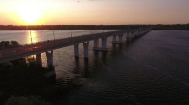 Yaz aylarında hareket eden bir drone ile gün batımında düz bir köprünün havadan çekilmiş Muhteşem kuş bakışı dnipro üzerinde kübik sütunlar üzerinde uzak köprü görünümü yaz aylarında güneş yolu ile çok renkli günbatımı nda onunla uçan bir drone
