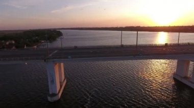 Yaz aylarında hareket eden bir drone pembe günbatımında büyük bir köprünün havadan çekilmiş Muhteşem kuş bakışı dnipro üzerinde kübik sütunlar üzerinde uzak köprü görünümü yaz aylarında güneş yolu ile çok renkli günbatımı boyunca uçan bir drone
