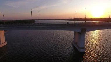 Yaz aylarında hareket eden bir drone altın gün batımında yüce bir köprünün havadan çekilmiş Harika kuş bakışı dnipro üzerinde kübik sütunlar üzerinde uzatılmış köprü görünümü yaz aylarında güneş yolu ile parıldayan gün batımında onu bir kenara uçan bir drone