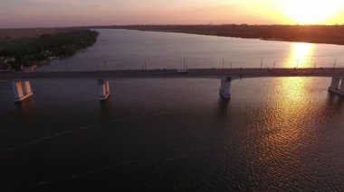 Yaz aylarında gün batımında Dnipro kapsayan düz beton köprünün havadan çekilmiş Aktif araç trafiği ve yaz aylarında parlayan gün batımında ona yaklaşan bir drone ile Dnipro üzerinde kübik beton sütunlar üzerinde büyük bir köprü heyecan verici kuş bakışı görünümü