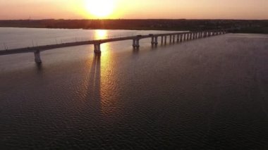 Altın bir güneş yolu ile Dnipro üzerinde güzel bir nehir köprüsü havadan çekim Üzerinde araba trafiği ve yaz aylarında Ukrayna'da sanatsal günbatımında görkemli bir güneş yolu boyunca uçan bir drone uzanmış düz bir köprü çarpıcı kuş bakışı görünümü