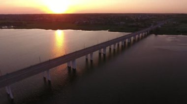 Yaz aylarında görkemli bir gün batımında Dnipro üzerinde uzak bir köprü havadan çekim Yeşil bankalar ile Dnipro nehri üzerinde yüce bir modern köprü güzel kuş bakışı görünümü, araba sürme ve yaz aylarında güneş yolu ile gün batımında parlayan su