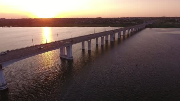 在灿烂的日落中覆盖Dnipro的长桥的空中拍摄令人印象深刻的鸟瞰图 一个拉伸的直桥与骑乘汽车加入Dnipro的黑暗码头在五彩日落与太阳路径在夏天 — 图库视频影像