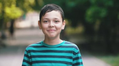 Mutlu brunet çocuk yaz güneşli bir günde yeşil bir sokakta neşeli bir şekilde gülümseyen Harika bokeh portre çizgili yeşil ve siyah t-shirt ayakta ve yaz aylarında güneşli bir günde yeşil sokakta gülümseyen kısa bir saç kesimi ile neşeli brunet çocuk.