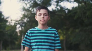 Cesur brunet çocuk gidiyor ve yavaş hareket muhteşem bokeh portre çizgili yeşil ve siyah t-shirt giden kısa saçlı küçük bir çocuğun yaz aylarında yeşil bir sokakta gidiyor ve gülümseyerek ve slo-mo yeşil bir sokakta hayatının tadını