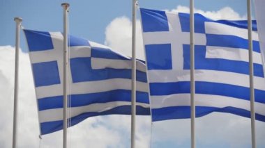 Yaz aylarında slo-mo'da bayrak direkleri üzerinde gök gökyüzünde çırpınan iki Yunan bayrağı, yaz aylarında güneşli bir günde güneşli bir günde yüksek bayrak direkleri üzerinde yalnız bulutlar ile açık mavi gökyüzünde uçan iki büyük Yunan bayrağının güzel görünümünde.