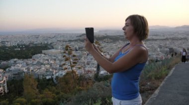 Yazın Atina 'da bir tepede dururken, güzel sarışın bir kadının akıllı telefonuyla fotoğraf çekişini etkileyici bir şekilde gösteren yatay olmayan Atina manzarasının fotoğrafını çeken sarışın kadından esinlendim. Panoramayı seviyor..