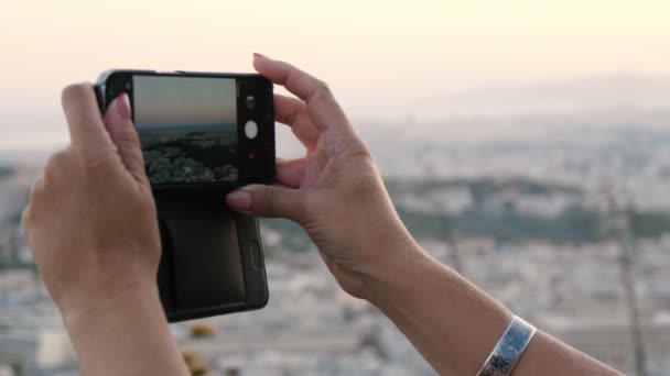 在夏日的一个阳光灿烂的日子里 女性手拿着智能手机拍照 手握现代智能手机 拍着无边无际的雅典风景 — 图库视频影像