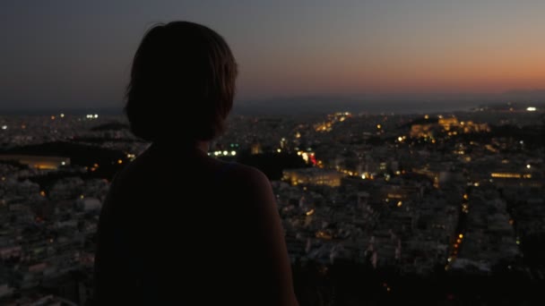 丘の上に立つ女性観光客を感動させ 夏にアテネの景色を楽しむ素晴らしいブロンドの女性の素晴らしいバックビュー丘の上に立っている袖のないブラウスにボブの散髪と夏に紫の夕日で古代の風景を見て — ストック動画