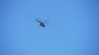 Askeri yeşil ve beyaz helikopter havada gezinen ve yavaş yavaş mavi havada uçan büyük askeri yeşil ve beyaz rotorcraft büyük askeri yeşil ve beyaz rotorcraft görünümü aşağı aşağı etkileyici uçan ve sonbaharda mavi gökyüzünde uçan. Atlamaya hazır paraşütçülerle dolu..