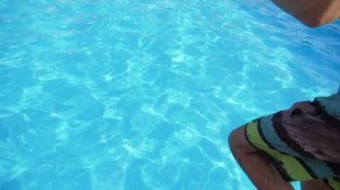 Neşeli adam slo-mo parlak suları ile bir yüzme havuzunda ilk ayak atlama renkli şort dalış ayakları sportif bir rakam ile genç bir brunet adam iyimser görünümü yavaş hareket te bir yüzme havuzunda parlayan açık mavi sularda ilk.