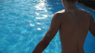 Slo-mo'da pırıl pırıl sularla bir yüzme havuzunda ilk kez kafa danat eden genç adam, yavaş çekimde bir yüzme havuzunda parlayan gök sularında bir serçe gibi dalış yapıyor sportif bir figüre sahip genç bir brunet adamının etkileyici görünümüyle.