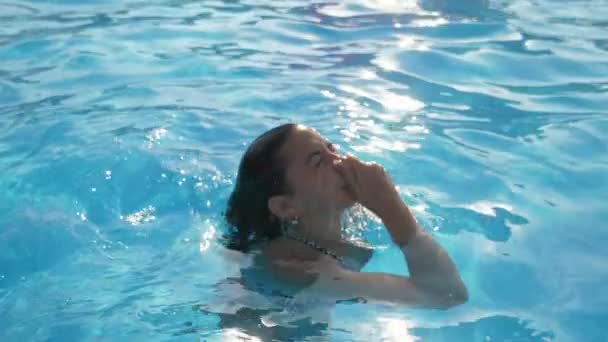 年轻女子从水中出来 保持她的鼻子在游泳池在Slo Mo原始视图一个美丽的年轻女子与长松散的头发浮出水面 并采取她的鼻子在一个戏水与闪闪发光的蓝色水在慢动作 — 图库视频影像