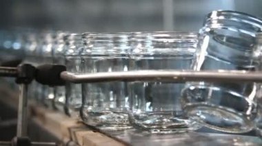Bir domates bitkisinin konveyör şeridinde hareket eden ve yaslanan cam kavanozlar modern bir domates üretim tesisinin geniş bir koridorunda içi boş cam bankaların yanıp sönen ve eğildiği komik bir yakın plan. Tekno ve neşeli görünüyor..