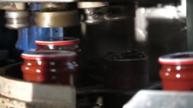 Domates bantları, bir fabrikada, yuvarlanan bir robotun altında metal bir şeritte hareket eden domates hamuru bankalarının yuvarlanan bir robot kapağının altında hızla koştuğunu ve yüksek teknoloji domates işleme tesisinde bir insanın elinin hızla koştuğunu gösteren neşeli bir görünüm içinde.. 