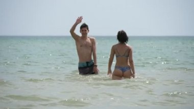 Güneşli bir günde, Karadeniz dalgalarında oynayan ve dans eden sevimli bir çift. Güneşli bir günde güneşli bir günde, şık ve gülümseyen kızıyla el sallayan ve el sallayan mutlu, sportif bir oğlanın görüntüsü.