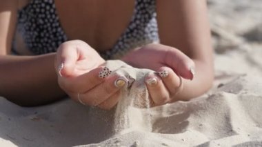 Kumla oynayan ve yazın deniz kıyısındaki bir tatil köyünde akarsu ile gezen kadın elleri zarif bir makyajla kumu alıyor, onu döküyor ve bir deniz tatil beldesinde onunla oynuyor. İlham verici ve iyi görünüyor..